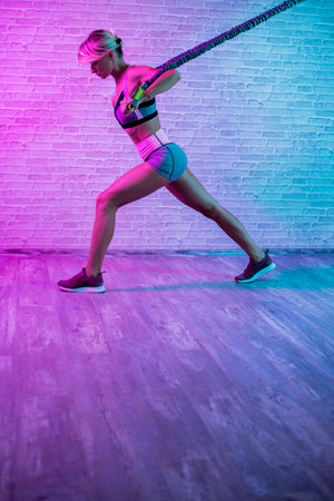 Fit young blonde woman workout with stretch bands in gym in neon lights.の写真素材