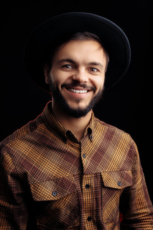 Handsome young bearded hipster in brown shirt smiling over black background.の写真素材