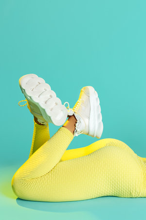 Close-up image of fit young brunette womans legs posing over turquoise background. Power and...