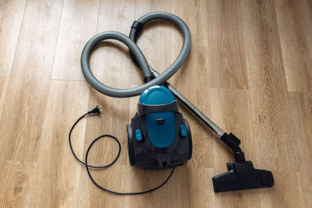 Modern blue vacuum cleaner on the wooden floor in living room. Heart Shape. Clean House Concept.