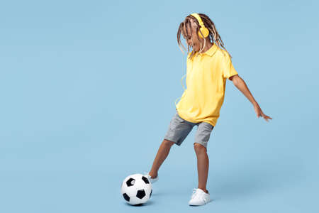 Sporty little boy with african dreads shoot soccer ball over blue background.の写真素材