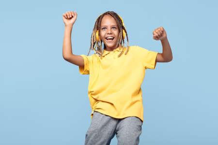 Gleeful little boy with african dreads listening music in headphones dancing over blue background.の写真素材