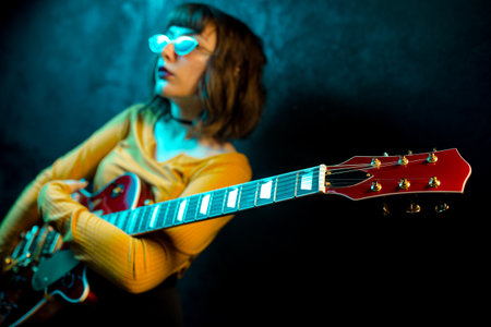 Fashion young hipster woman with curly hair with red guitar in neon lights. Rock musician posing with electrical guitar.の写真素材