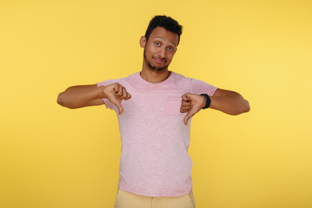 African american young man showing thumbs down over yellow background