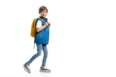 Full length image of a little boy with backpack walking over white background. Looking in camera