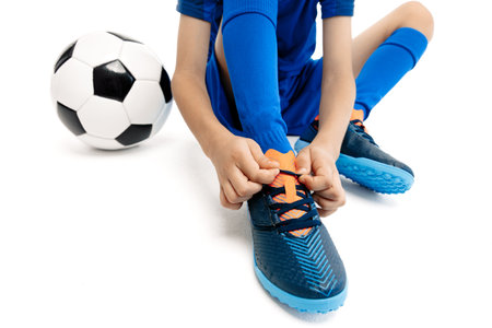 Close-up image of young boy in blue sport outfit tying his shoelaces on the floor on white backgroundの写真素材