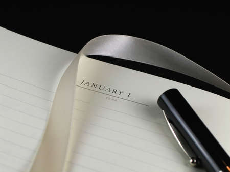 A blank sheet of paper with lines, a silk ribbon bookmark and a black pen against a black background
