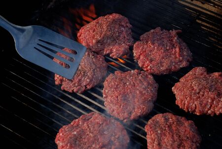 Seven hamburger patties cooking on a grill with a silver spatula in the frameの写真素材