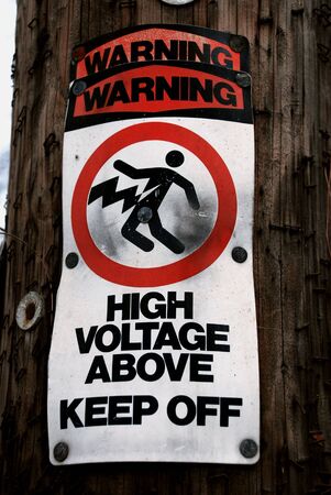 A weathered and worn sign warning people of the high voltage power lines aboveの写真素材