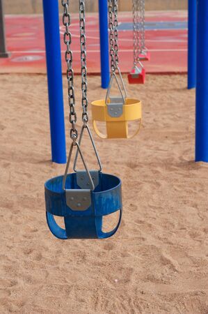 Colorful Empty Swings standing still with chainlink on a playground with sandの写真素材