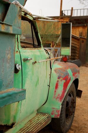 A rusty old truck with patches of green and red paint in a dirt lotの写真素材