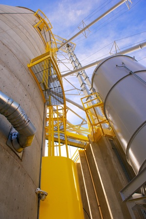 Vertical shot of towering grain silos made of concrete with metal conduits and yellow access areas at a food processing plantの写真素材