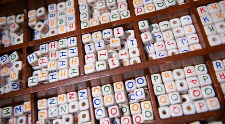 Wooden tray keeps white ceramic beads with the alphabet on them organizedの写真素材
