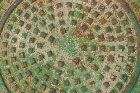 Oxidized man hole cover with rust stains and sand that includes a pattern of raised squares