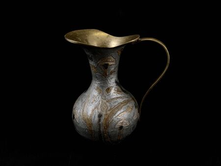 Copper antique vase on a black background. Copper dishes with patterns and ornaments. Metal decanter for decoration in the house.の写真素材