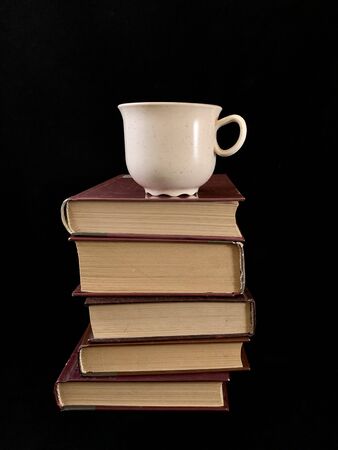 Closed books and a cup of coffee on a black background. A cup of tea near the hardback book.の写真素材