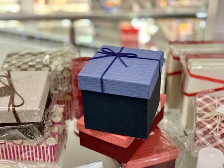 A gift wrapped in a square box with a ribbon on the background of other gifts. Multicolored gift...