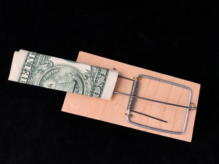 Dollars in a mousetrap on a black background. Wooden trap with bait and mechanism for rats and mice....