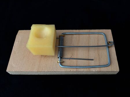 Free cheese in a mousetrap on a black background. A wooden trap with a bait with a metal mechanism...