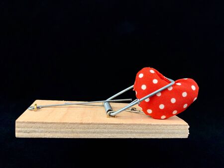 Heart in a mousetrap on a black background. Concept: Trap with a heart, Love as a bait. Valentine's...