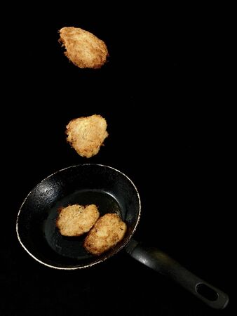 Potato pancakes in the cooking process. Fried pancakes in an old pan, on a black background. Cooked pies in a pan in sunflower oil.の写真素材