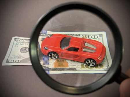 Toy car and hundred dollar bill. Children's model of a modern red car. Concept: buying, selling,...