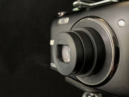 Digital camera with a small lens on a black background. Concept: home photo shooting, photo equipmentの写真素材