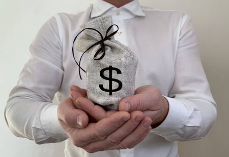 A bag with a dollar sign in the hand of a businessman. A man holds a burlap in his hands. A business man shows a sign of wealth. Concept: investment, material success, incomeの写真素材