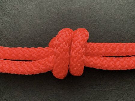 Knot on a bright nylon rope, black background. Double rope tied. Concept: interconnectedness,...