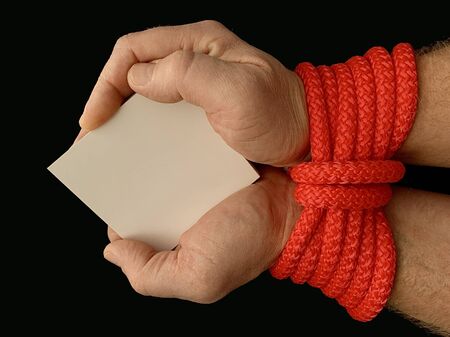 Hands tied with a rope, on a black background. Tied hands are holding a note with the inscription. Concept: message, slavery, addiction, messageの写真素材