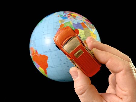Toy car in hand on a background of the globe. Man with a car model, on a black background. A man...