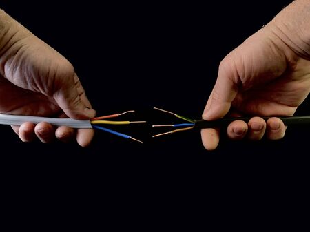 Open copper wires in a male hand. Electro wiring in hands, on a black background. Electrician...