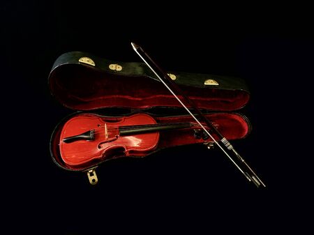 Decorative violin with case, on a black background. Bowed musical instrument. Toy violin with strings and bow.の写真素材