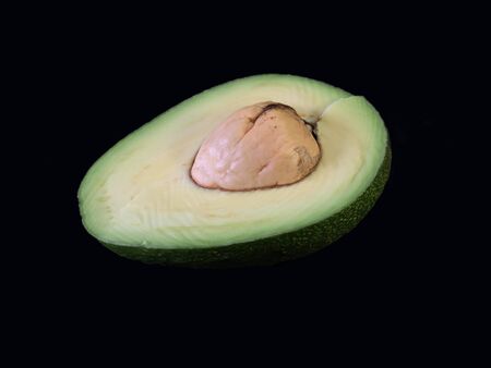 Slice of green avocado isolated on a black background. Ripe avocado with bone, in a cut. Half an...