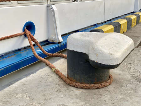 The ship's rope is tied to a post in the dock. The ship is moored to the shore. A thick rope keeps...