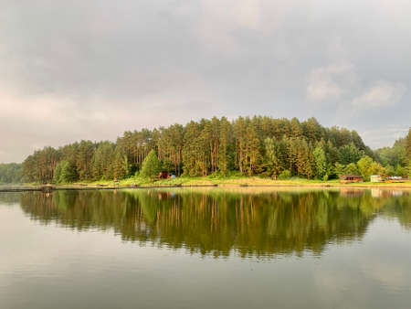 Trees are reflected in the water of the lake. Evening landscape, a small pond in the forest. Reflection of the blue sky and trees in a park reservoir. Sunset on a pond in the middle of nature.の写真素材