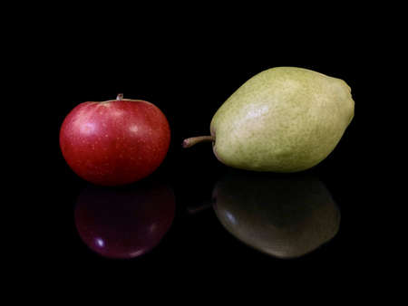Green ripe pear and apple on a black background. Fruit of fruit trees. Pears and apples are reflected on the glass. Concept: autumn fruits, useful natural vitamins.の写真素材