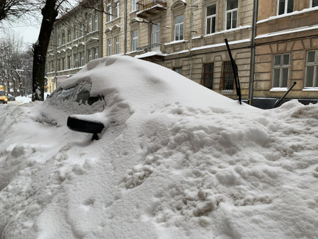 The car was covered with snow in the parking lot. Cars under a large layer of snow. Snowfall on the streets of a European city.の写真素材
