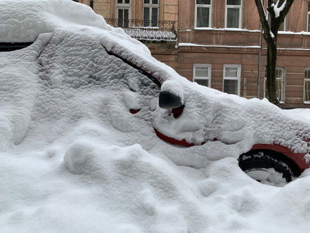 The car was covered with snow in the parking lot. Cars under a large layer of snow. Snowfall on the streets of a European city.の写真素材