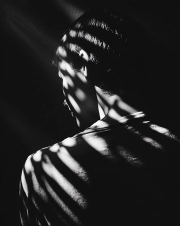 Silhouette of a person with light patterns against a dark background creating dramatic shadows in a dimly lit spaceの素材