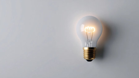 Bright light bulb glowing against a neutral background, symbolizing innovation and creativity in modern designの素材