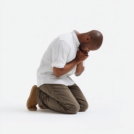 Man kneeling in a prayerful posture, expressing deep contemplation in a minimalist, bright indoor space during daylight hoursの素材