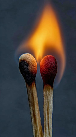 Two lit matches ignite a captivating flame against a dark backdrop, showing the beauty of fire and light in an artistic moment of contrastの写真素材