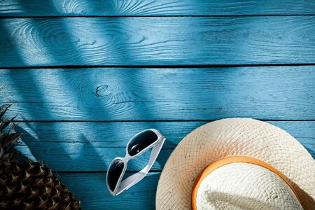 A hat, sunglasses and pineapple on a blue wooden boards seen from above.の写真素材