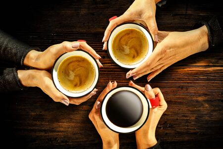 Young female manicured hands holding cups of coffee with fresh foam on dark rustic wooden table background. Free space for your decoration, copy space, top view, flat photo. Cold winter Christmas time.の写真素材