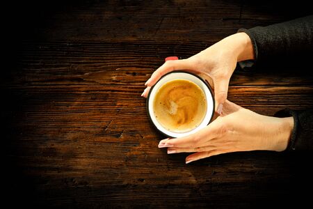 Young female manicured hands holding cups of coffee with fresh foam on dark rustic wooden table background. Free space for your decoration, copy space, top view, flat photo. Cold winter Christmas time.の写真素材