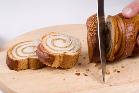 A kitchen knife slicing a loaf of a long bread on a preparation board. Lots of crumbs on the board.