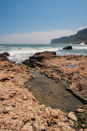 Ocher rocky shore with Cape of San Antonio in the background in Las Rotas, Denia.の写真素材