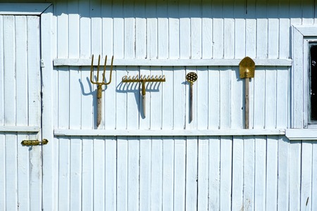 Tools for working in the garden are attached to the wooden wall painted white paint. Forks, rakes, shovels, sieve. Work in the summer garden.の写真素材