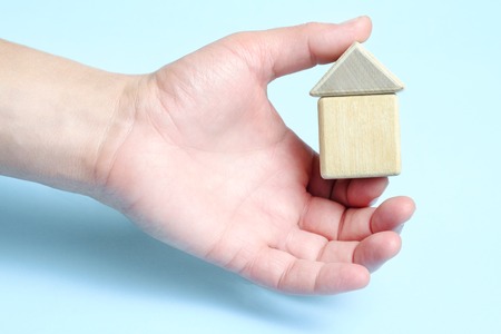 Toy house made of wooden cubes in male hand. Isolated on blue background.の写真素材